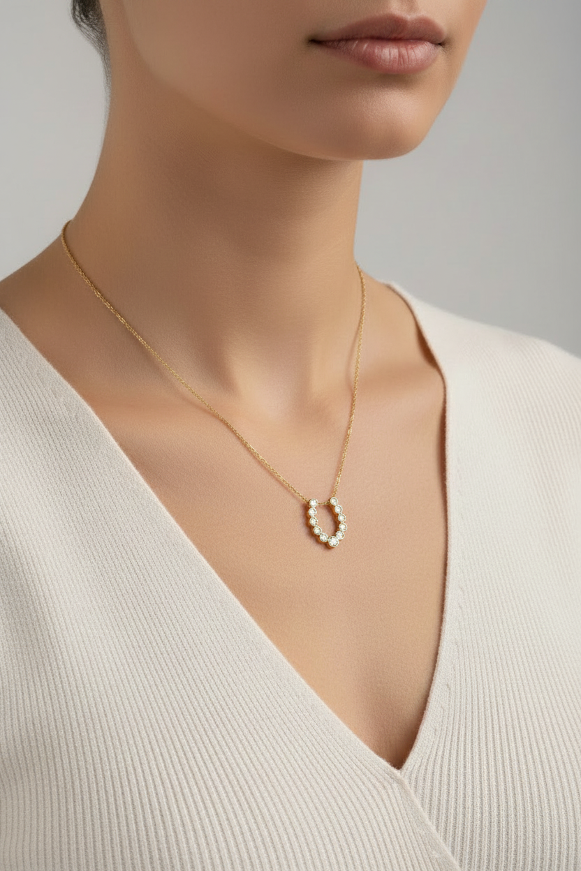 A gold necklace with a delicate chain and a U-shaped pendant featuring small round clear stones and one larger central clear stone, shown on a plain white background.