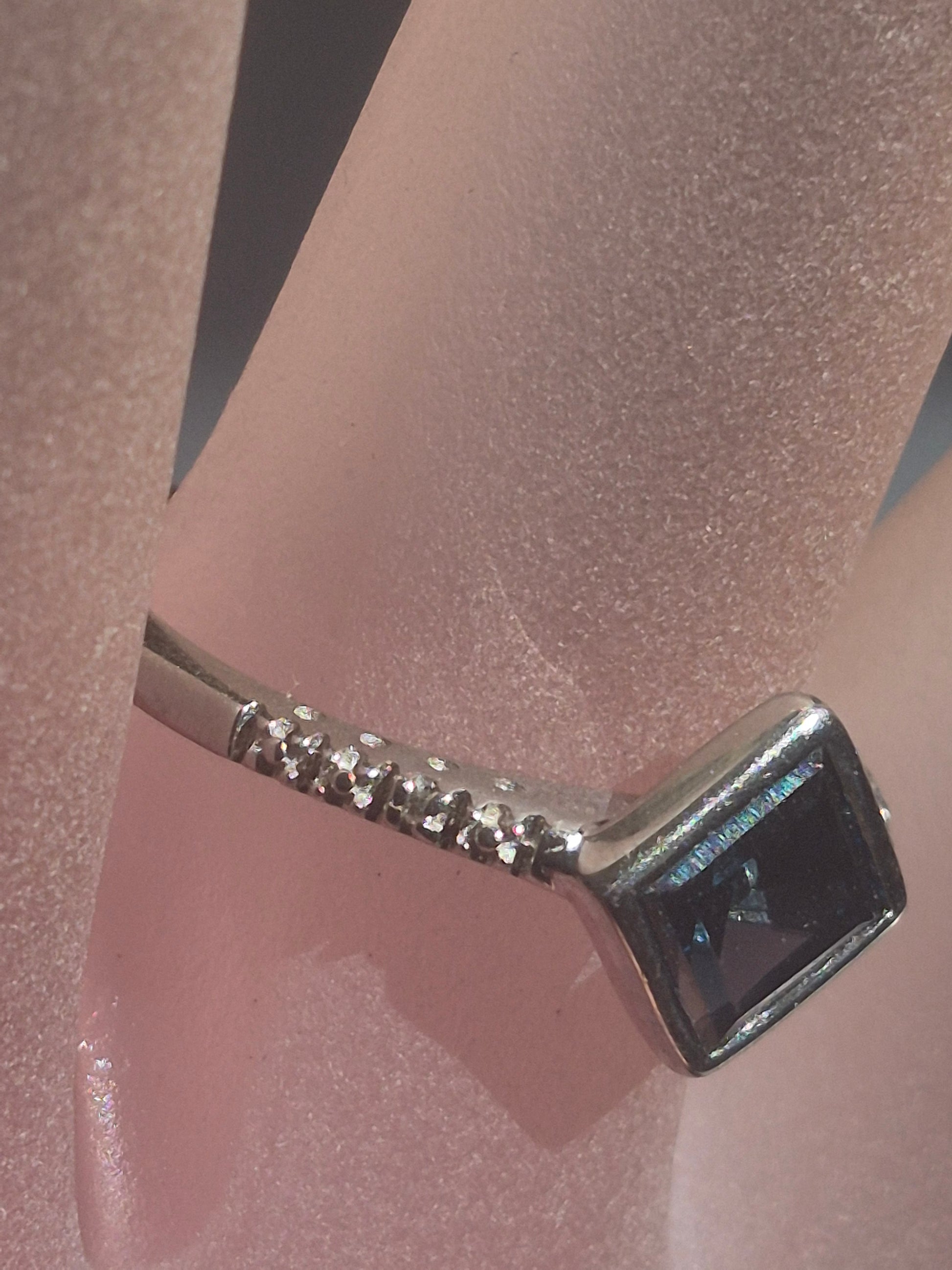 A silver-toned ring with a square dark blue gemstone, displayed on a pink textured ring stand.