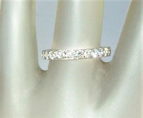 A silver-tone eternity ring set with small clear round-cut stones, displayed on a cream-colored satin ring stand.