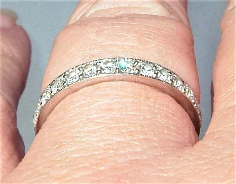 A close-up of a silver-toned eternity band ring set with small clear stones, worn on a finger.