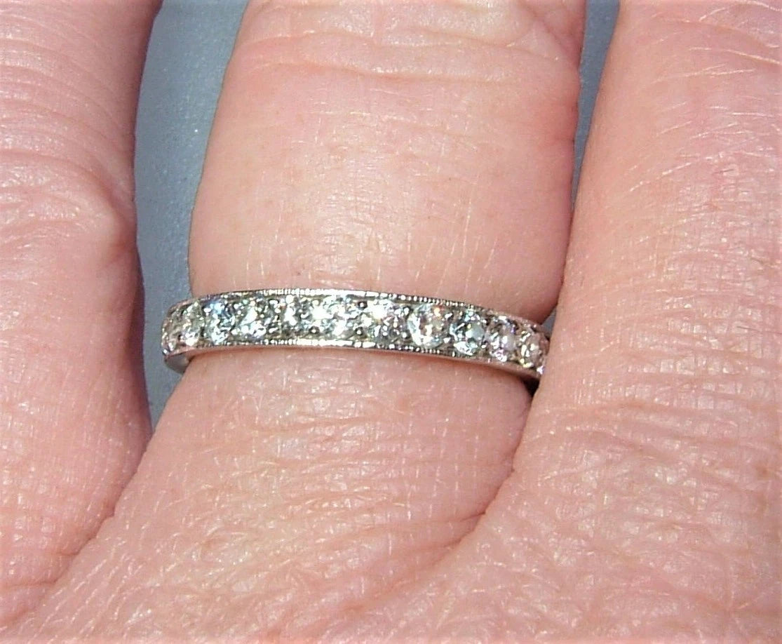 A close-up of a silver eternity ring with small clear stones set in a person's finger.
