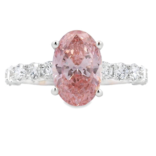 An oval-cut pink diamond ring set in a silver-colored band with small clear stones on either side, shown against a plain white background.